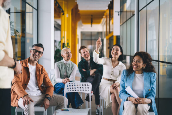 Group of happy multiethnic colleagues in casual clothes smiling and gesturing while having conversation about marketing strategy during meeting at work together on modern office