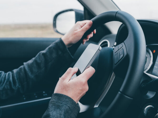 Texting and driving is dangerous behavior in traffic, close up of female hand typing text message on mobile phone while traveling through countryside with her car