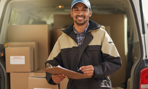 Portrait of a smiling delivery man standing in front of his van holding a package.