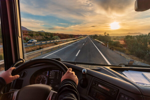 View from the driver's seat of a truck of the highway and a land View from the driver's seat of a truck of the highway and a landscape of fields at dawn.