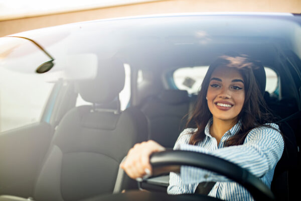 Beautiful young happy smiling woman driving her new car at sunse Beautiful young happy smiling woman driving her new car at sunset. Woman in car. Close up portrait of pleasant looking female with glad positive expression, woman in casual wear driving a car