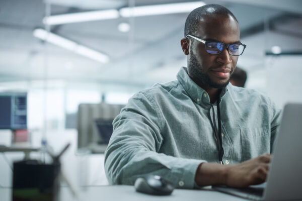 Modern Office: Portrait of Motivated Black IT Programmer Working on Laptop Computer. Male Specialist Create Website, Software Engineer Develop App, Program, Video Game. Stress Free Inclusive Space