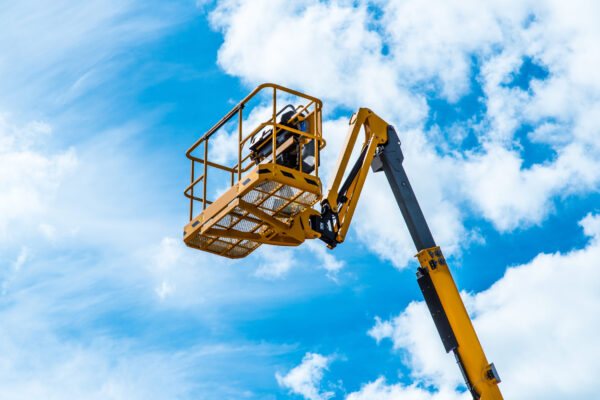 Hydraulic lift platform with bucket of yellow construction vehicle, heavy industry, blue sky and white clouds on background