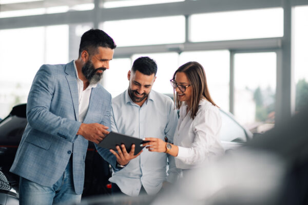 Professional car dealer advising satisfied couple in showroom. In a sleek car showroom, a professional dealer offers advice and insight to an intrigued couple, enhancing customer satisfaction and decision-making with expert knowledge.